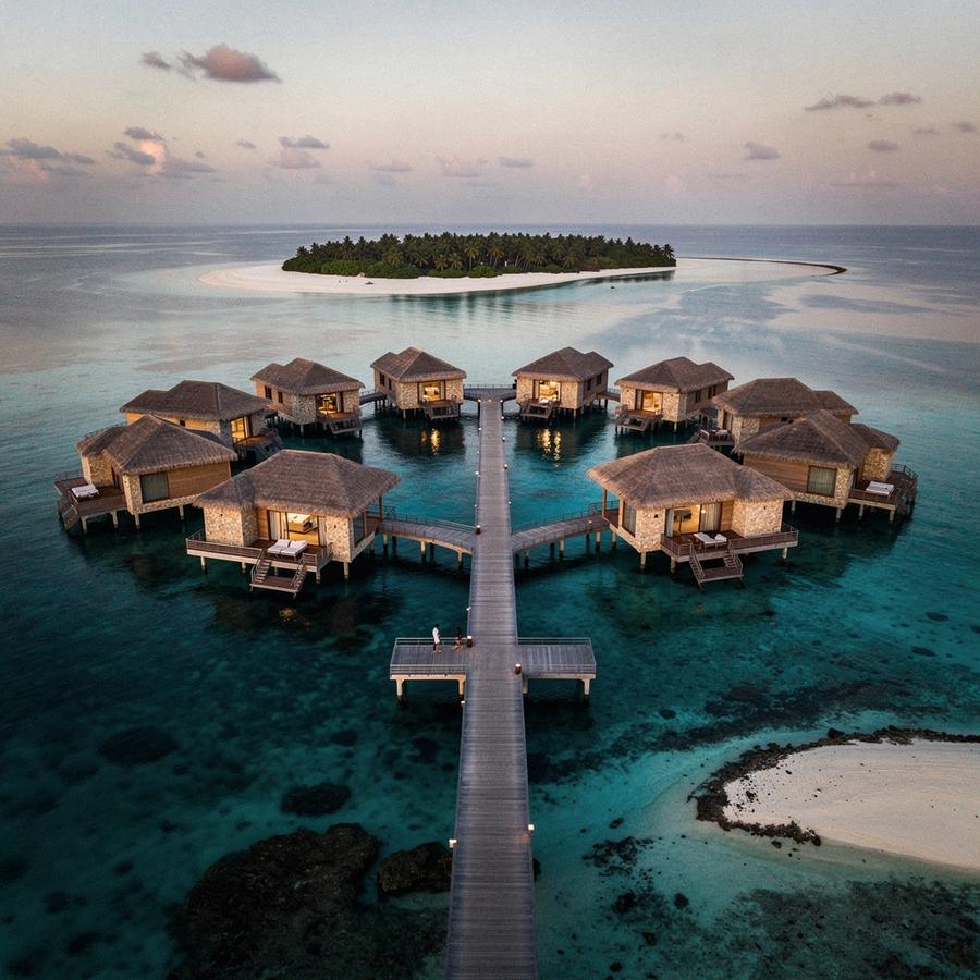 Over-water villas on a Maldives lagoon at dusk, seen from the arrival jetty